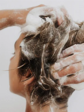 Personne lavant délicatement ses cheveux avec un shampooing pour cuir chevelu sensible riche en mousse douce